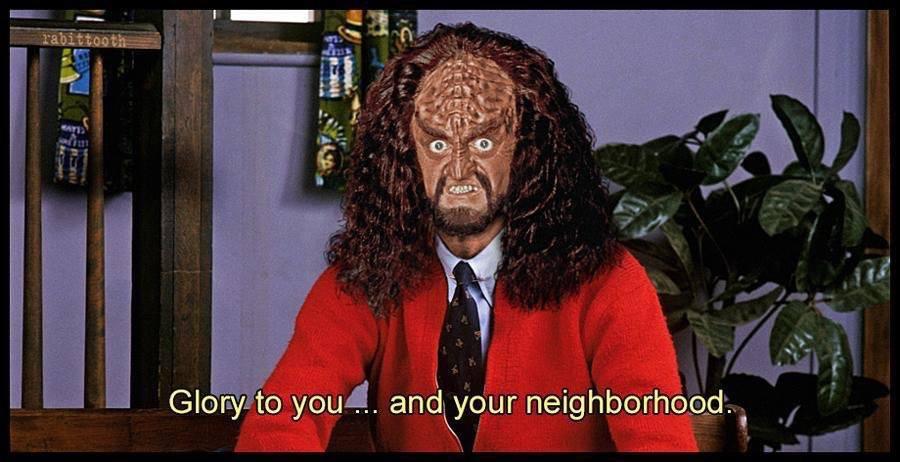 Gowron from Star Trek Next Generation in Mr. Roger's living room wearing a red sweater. The caption reads, "Glory To You And Your Neighborhood"