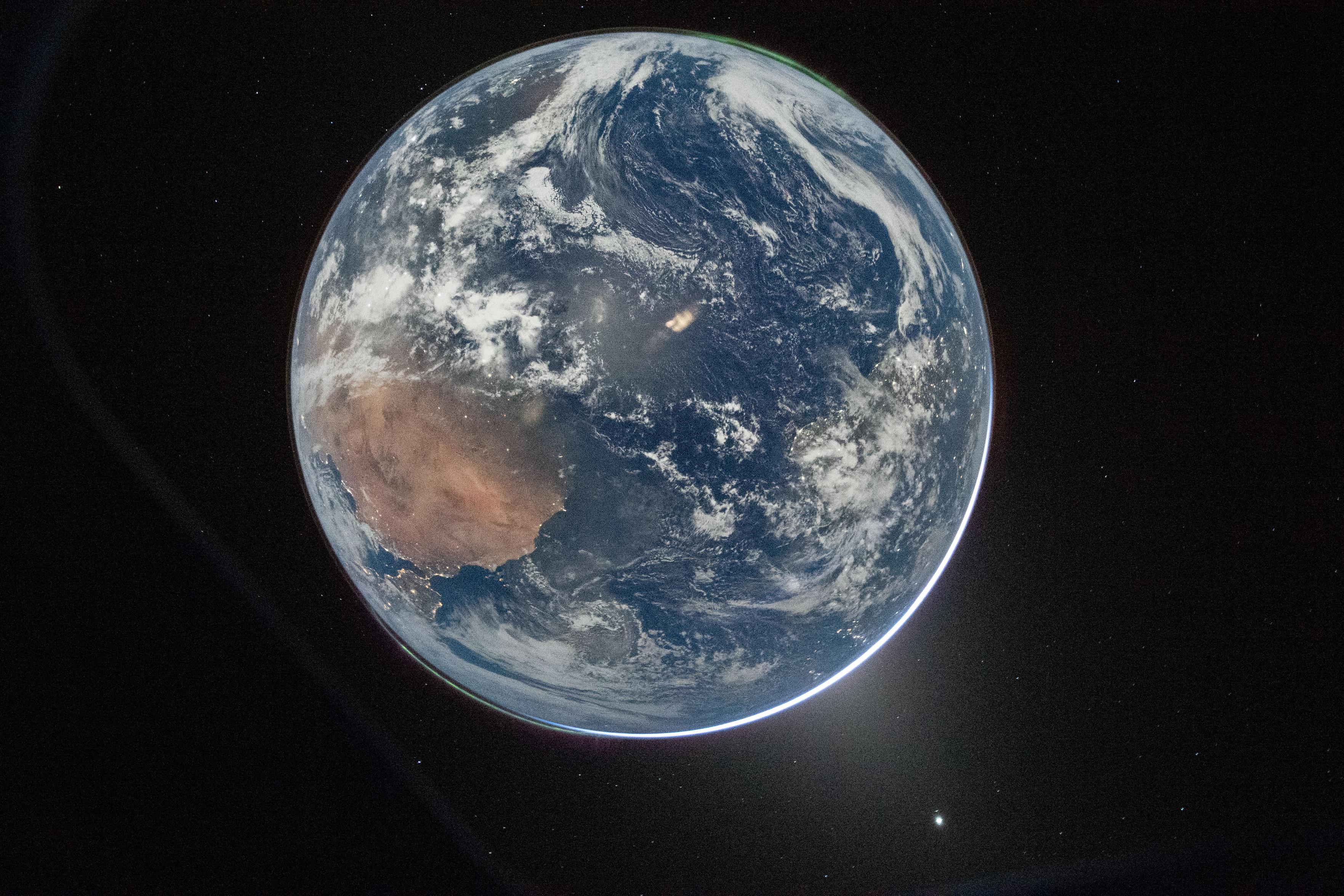 A picture of the Earth from space illuminated by the full Moon – it looks like daylight, but this is the night side of the planet, not the day side. There are city lights on the continents and a green aurora towards the north and south poles, plus a faint rim of upper atmosphere airglow as well. You can also see a faint dark rim of the Artemis II window frame and the zodiacal light (probably).